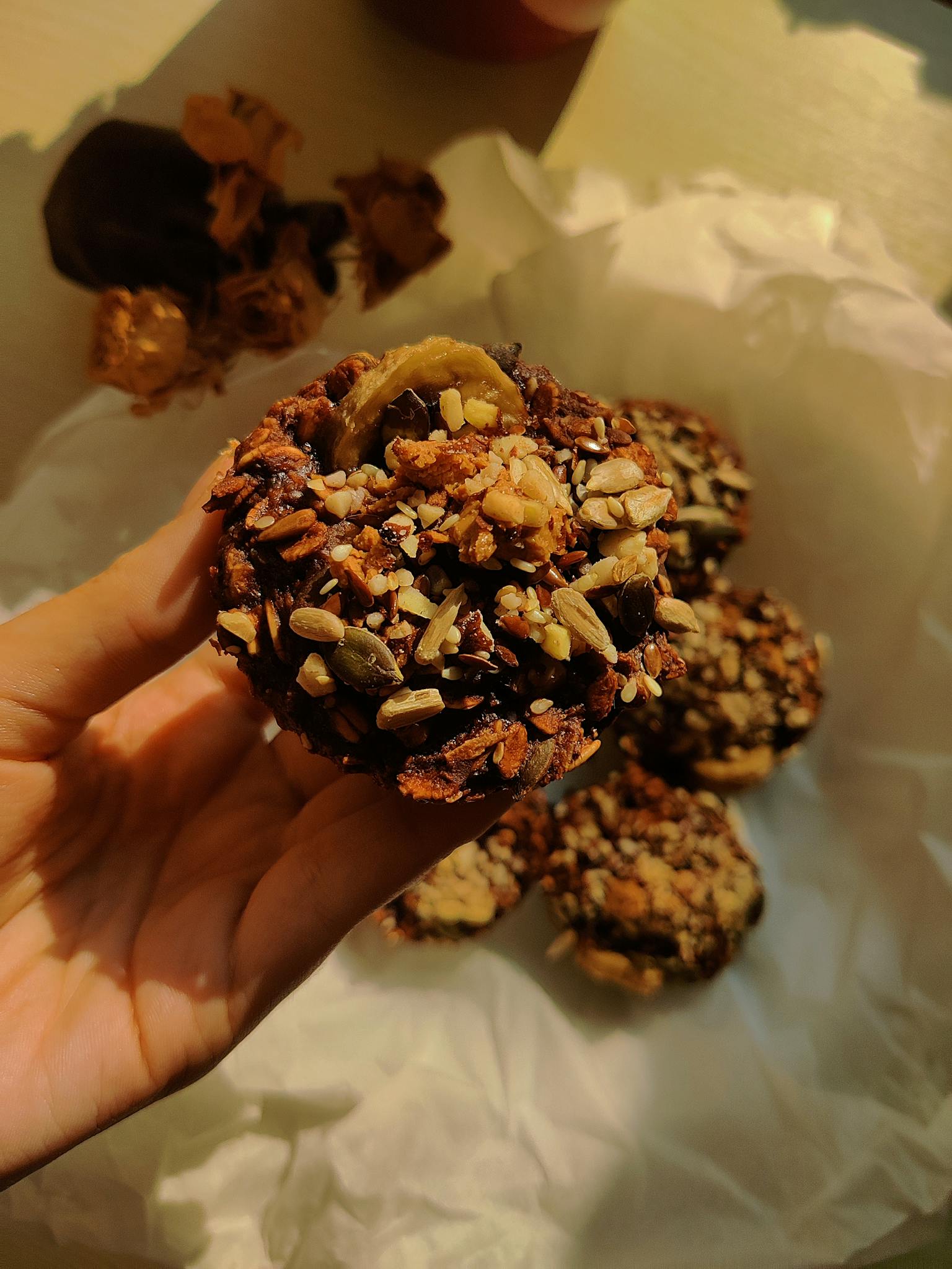 Close-up of a hand holding a homemade nut and seed cookie in warm lighting.